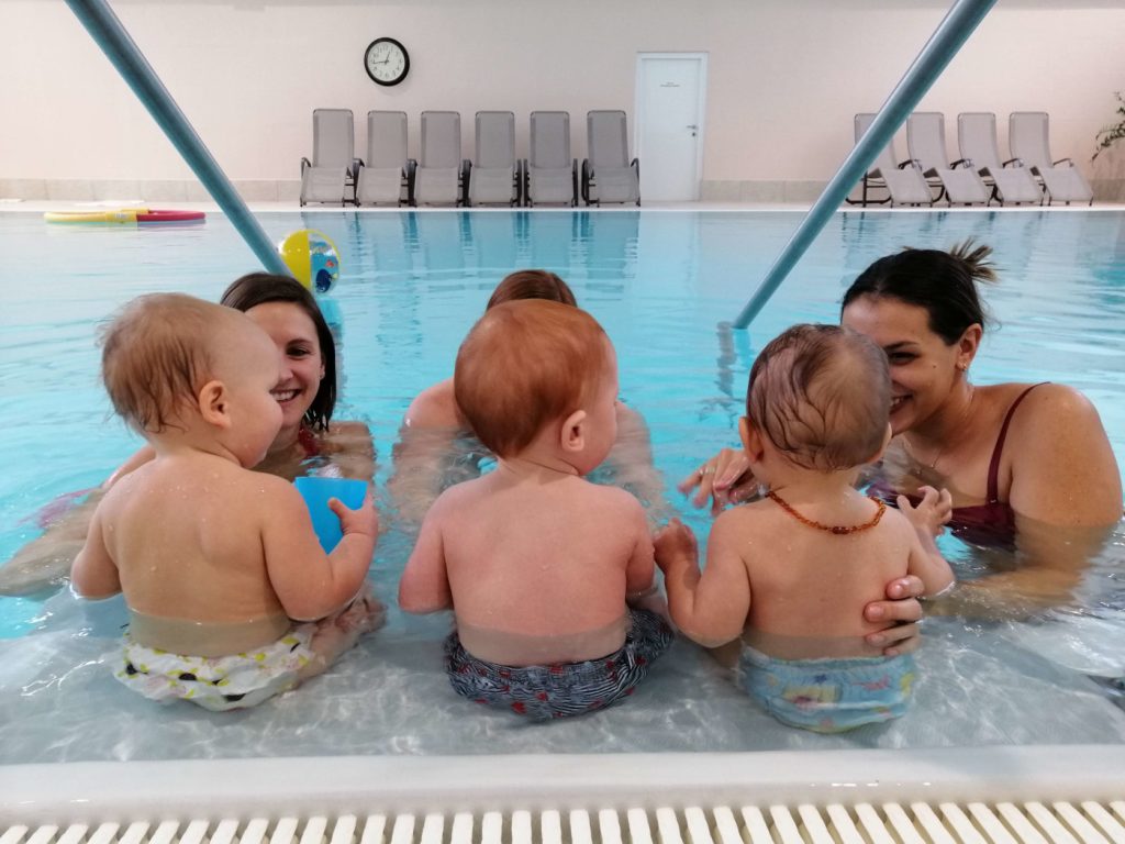 Drei Babys sitzen beim Babyschwimmen mit ihren Müttern am Beckenrand