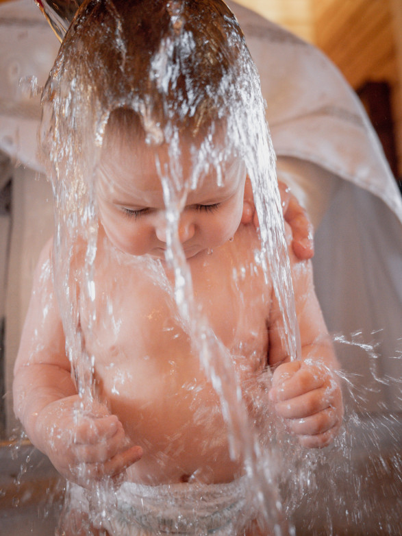 Baby unter einem Wasserstrahl beim Babyschwimmen