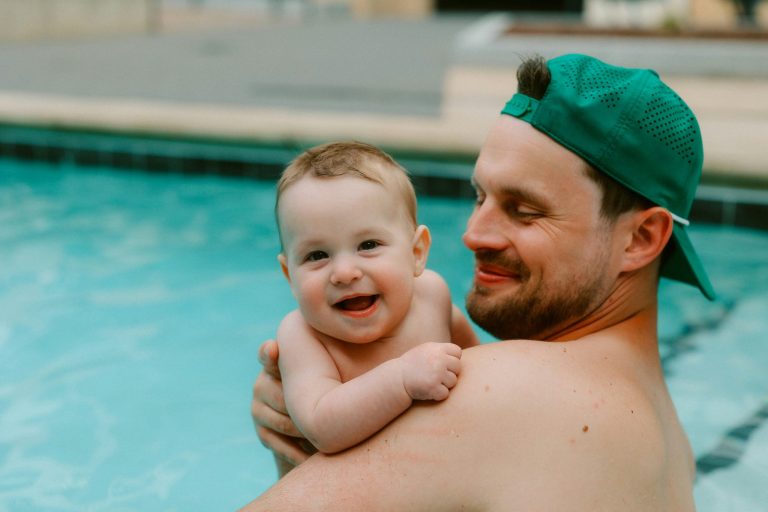 Vater hält lachendes Baby im Schwimmbecken